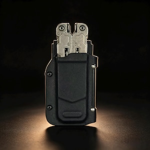 May include: A silver multi-tool partially inserted into a black moulded plastic sheath. The sheath features a vertical belt clip, two visible screws on the left side, and a metallic rivet on the right side, securing the tool in a compact vertical position.