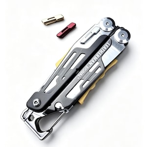 Op de afbeelding: Een Leatherman Signal multitool in gesloten positie met een grijs en zwart frame, zilverkleurige hardware en gele accenten. Het gereedschap is voorzien van een karabijnhaak en wordt vergezeld door twee kleine, losse rechthoekige inzetstukken in goud en rood.