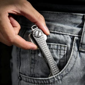 May include: A metallic silver key organiser featuring a textured grid pattern on the front surface and a large flat-head screw mechanism at the top. The device is designed to hold multiple keys in a compact, streamlined, and organised fashion.