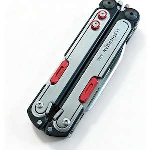 Op de afbeelding: Een gesloten Leatherman Arc multitool met een behuizing van geborsteld zilverkleurig metaal, zwarte accenten en felrode vergrendelingsknoppen. De tekst LEATHERMAN ARC staat duidelijk op de zijkant, samen met zichtbare schroeven.