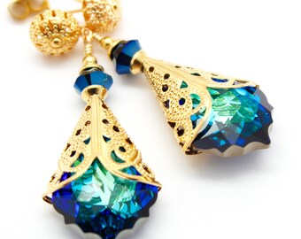 May include: A pair of gold-toned earrings with intricate filigree detailing. Each earring features a faceted, teardrop-shaped pendant in shades of blue and teal. The earrings have a post-back closure and a decorative ball at the top.