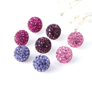 May include: Assortment of six sparkly round buttons in shades of pink, purple, and lavender. The buttons are made of rhinestones and have a silver backing.