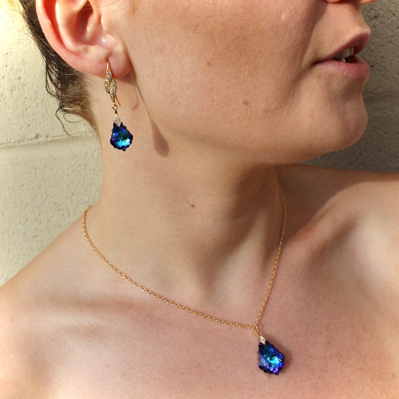 Pode incluir: Um colar de corrente de ouro com um pingente em forma de l&aacute;grima com um cristal azul. O pingente &eacute; acentuado com um cristal transparente menor. O colar &eacute; combinado com brincos combinando com gotas de cristal azul em forma de l&aacute;grima.