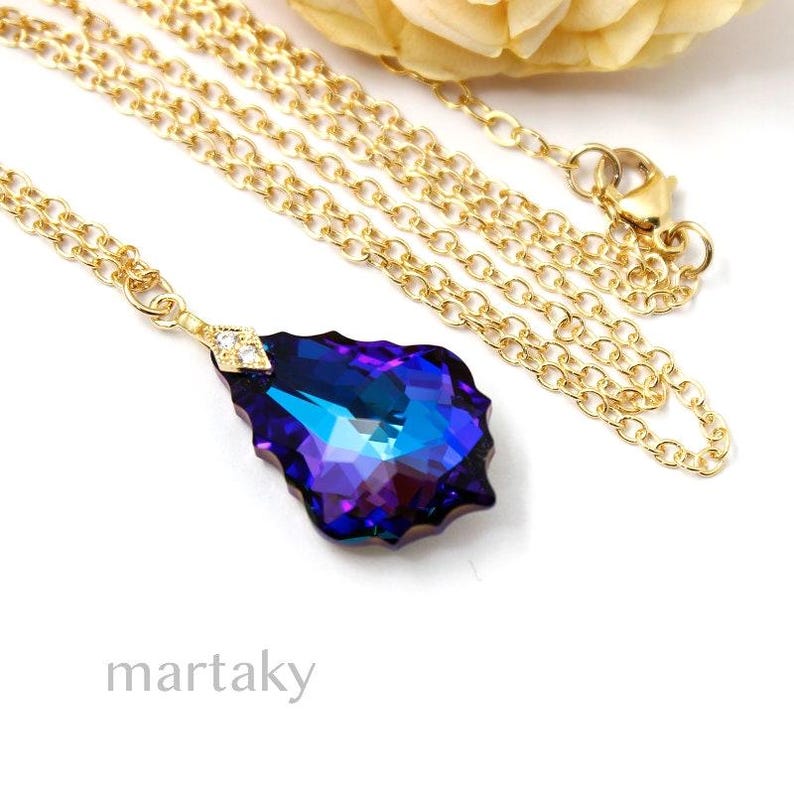 Pode incluir: Um colar de corrente de ouro com um pingente em forma de l&aacute;grima. O pingente &eacute; um cristal azul escuro e roxo com um acento de cristal transparente na parte superior.