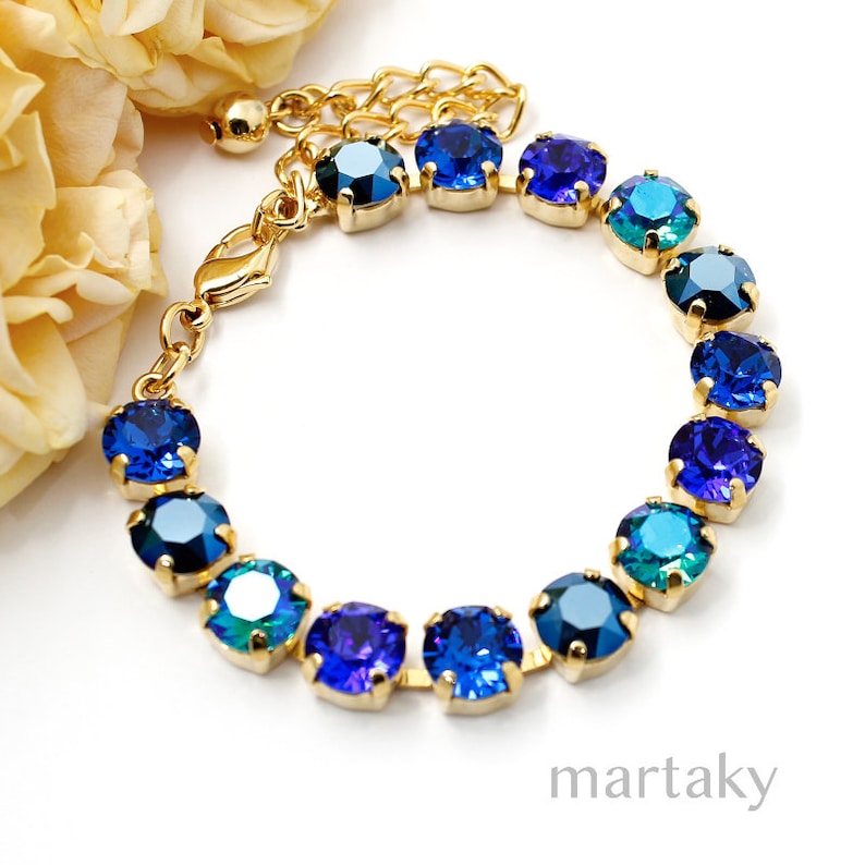 Puede incluir: Una pulsera dorada con una serie de piedras preciosas azules redondas en varios tonos. Las piedras est&aacute;n engastadas en biseles dorados individuales y conectadas por una delicada cadena dorada. La pulsera es ajustable y tiene un cierre de langosta.