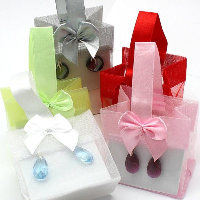 Puede incluir: Cuatro peque&ntilde;as bolsas de regalo en varios colores: blanco, rosa, rojo y plateado. Cada bolsa tiene un asa de cinta y un lazo decorativo. Las bolsas contienen un par de pendientes con gemas en forma de l&aacute;grima.