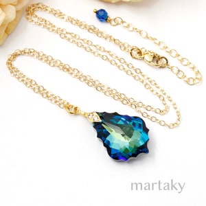 Puede incluir: Un collar dorado con un colgante grande en forma de l&aacute;grima. El colgante presenta tonos azules y verdes, con un peque&ntilde;o detalle de diamante. La cadena es fina y el cierre es visible. La palabra "martaky" est&aacute; en la parte inferior.