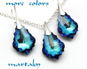 May include: A silver necklace and earrings set with teardrop-shaped blue crystal pendants. The crystals have a gradient of blue shades, from dark blue to light blue.