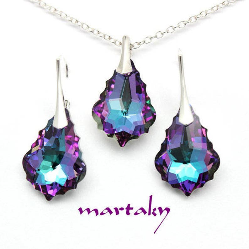 May include: A silver necklace and earrings set with iridescent purple and blue teardrop-shaped crystals. The crystals have a faceted design.