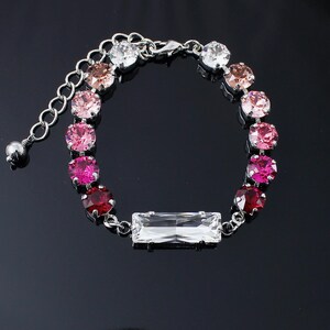 May include: A silver bracelet with a gradient of pink, red, and clear crystals. The bracelet has a clear rectangular crystal in the center.