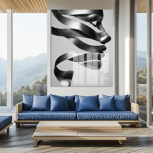 May include: Black and white abstract art print featuring a face composed of ribbon-like shapes. The artwork is displayed above a blue sofa and wooden coffee table on a patio with a mountain view.