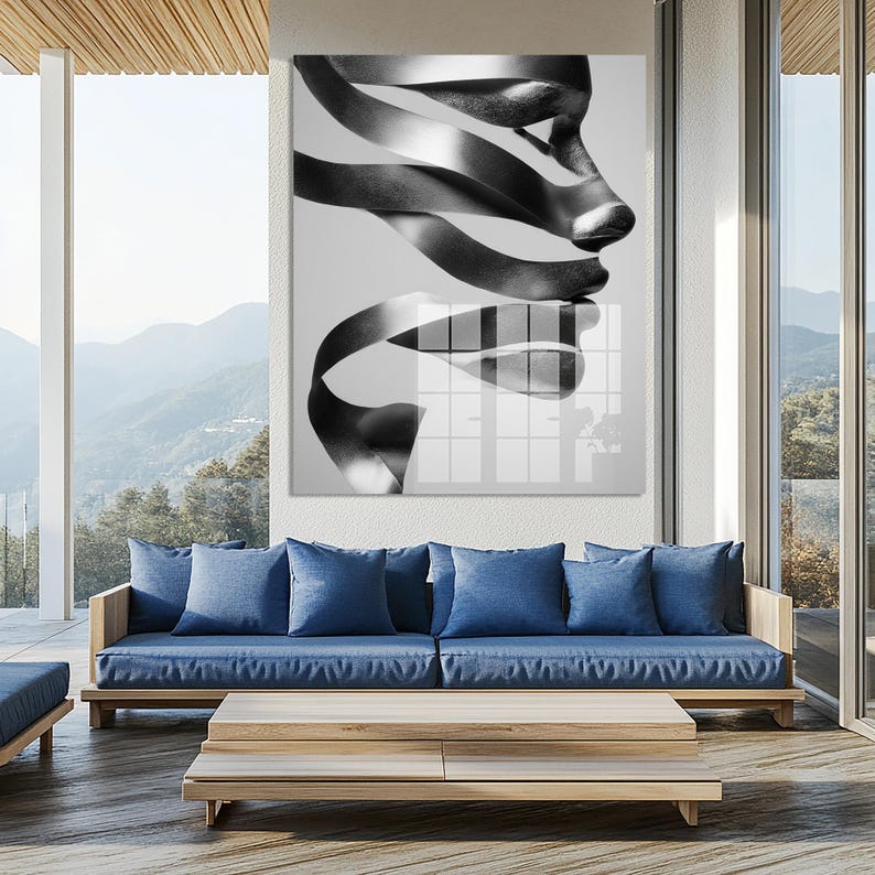 May include: Black and white abstract art print featuring a face composed of ribbon-like shapes. The artwork is displayed above a blue sofa and wooden coffee table on a patio with a mountain view.