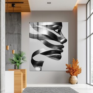 May include: Large black and white abstract art piece featuring a profile of a face with ribbon-like elements. The artwork is displayed on a wall in a modern interior setting, with a neutral color palette and natural light.
