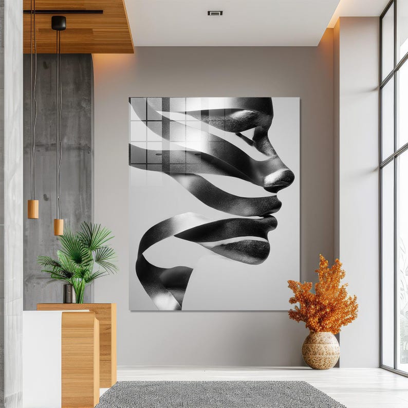 May include: Large black and white abstract art piece featuring a profile of a face with ribbon-like elements. The artwork is displayed on a wall in a modern interior setting, with a neutral color palette and natural light.