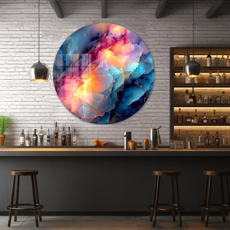 Pu&ograve; includere: Un'opera d'arte murale rotonda con un design astratto. L'opera presenta una miscela di colori, tra cui blu, rosa e giallo, con accenti dorati. L'opera &egrave; esposta su un muro di mattoni bianchi sopra un bar con sgabelli.