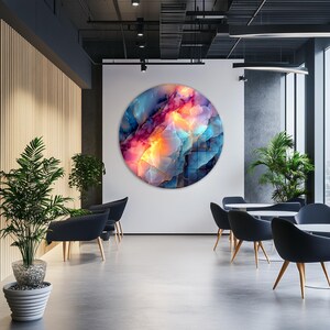 Pu&ograve; includere: Un'opera d'arte astratta circolare di grandi dimensioni con una vivace miscela di colori, tra cui blu, rosa e giallo, &egrave; appesa a una parete bianca. L'opera d'arte &egrave; il punto focale di uno spazio interno moderno, completato da sedie, tavoli e piante in vaso.