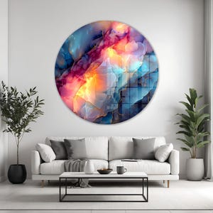 Pu&ograve; includere: Un'opera d'arte murale rotonda con un design astratto dai colori vivaci. Presenta una miscela di blu, rosa, arancione e oro, creando un effetto visivo dinamico. L'opera &egrave; appesa a una parete bianca sopra un divano bianco.