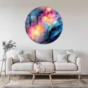 Pu&ograve; includere: Una grande opera d'arte murale rotonda con un design astratto. L'opera presenta una miscela di colori, tra cui blu, rosa e giallo, con accenti dorati. &Egrave; montata su una parete bianca sopra un divano beige.