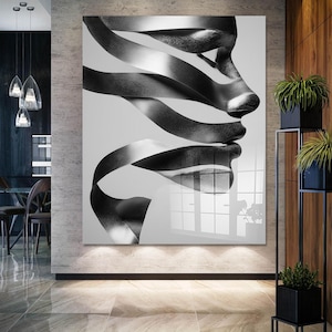 May include: Black and white abstract art print featuring a profile of a face created from flowing ribbons. The artwork is displayed on a large, glossy panel, creating a modern and artistic statement piece for interior decor.