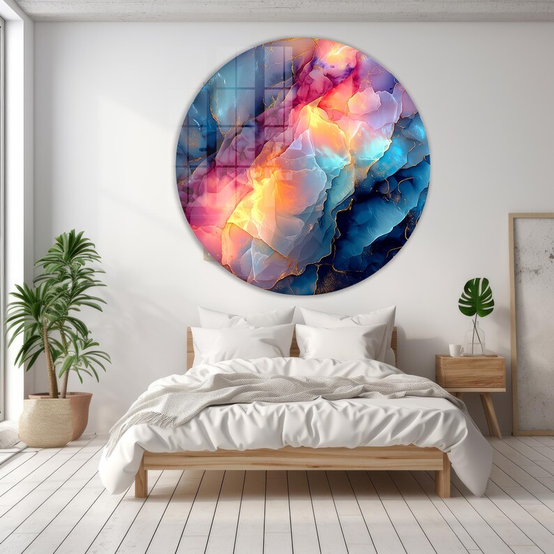 Pu&ograve; includere: Un'opera d'arte murale rotonda con un design astratto. L'opera presenta un vivace mix di colori, tra cui blu, rosa, arancione e oro. Il design assomiglia a una vista ravvicinata di una formazione di gemme. L'arte &egrave; montata sopra un letto.