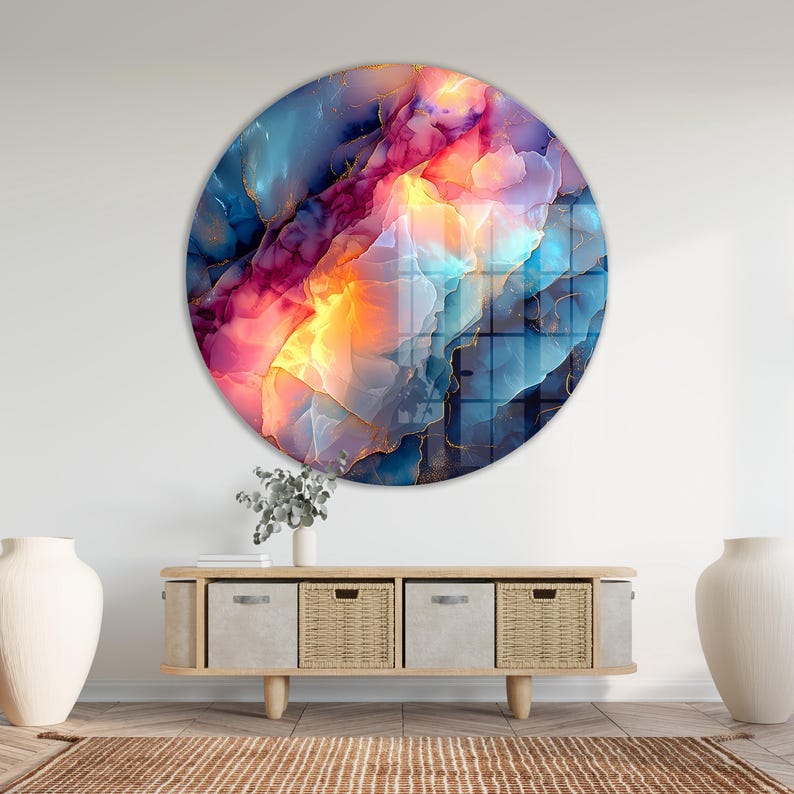 Pu&ograve; includere: Un'opera d'arte murale rotonda con un vivace design astratto. L'opera presenta una miscela di colori, tra cui blu, rosa, arancione e oro, creando un effetto visivo dinamico e accattivante. &Egrave; esposta su una parete bianca sopra un mobile in legno.