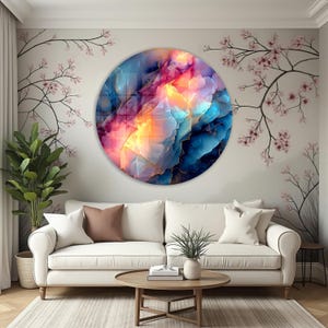 Pu&ograve; includere: Un'opera d'arte murale rotonda con un vivace design astratto nei toni del blu, rosa e giallo. L'opera &egrave; appesa sopra un divano bianco e un tavolino di legno. La stanza ha un'atmosfera moderna e ariosa.
