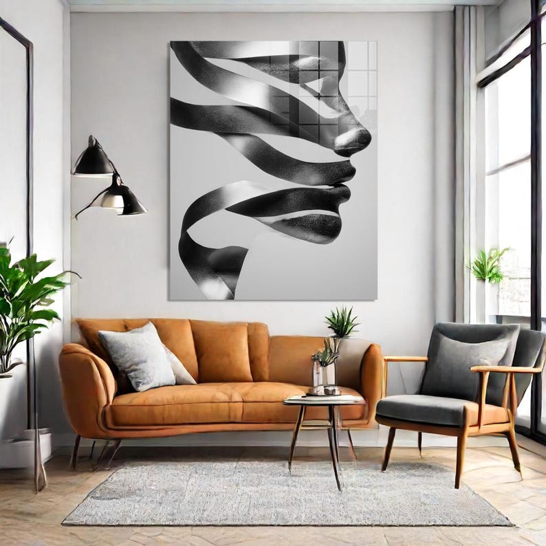 May include: A large black and white abstract art piece depicting a profile of a face with ribbon-like shapes. The artwork hangs above a brown leather sofa, a gray armchair, and a small side table.