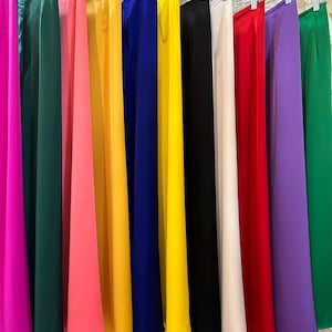 May include: A display of 12 long, flowing skirts in various colors, including purple, green, pink, yellow, blue, black, white, red, and lavender. The skirts are hanging on hangers and are arranged in a row.