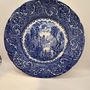 Puede incluir: Plato de porcelana azul y blanco con un borde decorativo y una escena de un castillo y un río con personas en un barco.