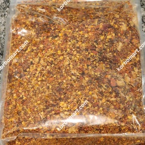 May include: A clear plastic bag filled with a mixture of dried red peppers, seeds, and other spices. The bag is sealed and has the text "korbomart.com" printed on it.