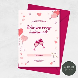 以下が含まれることがあります： ピンクと白のカードとピンクの封筒。カードにはハートのデザインと「LOVE IS IN THE AIR Will you be my bridesmaid?」というテキストが書かれており、その下に日付と住所が記載されています。