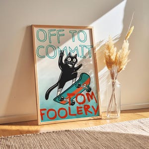 Peut inclure: Une affiche encadrée avec un chat noir de dessin animé sur un skateboard, avec le texte "OFF TO COMMIT TOM FOOLERY". Le chat fait le signe de la paix. Le fond est un dégradé bleu et blanc. Le cadre est en bois clair.