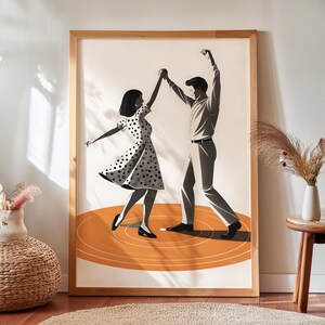 Puede incluir: Un cuadro enmarcado con una pareja bailando. La ilustración en escala de grises muestra a una mujer con un vestido de lunares y un hombre con una camisa abotonada. Bailan sobre un círculo naranja, dentro de un marco de madera.
