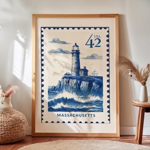 Puede incluir: Una impresión enmarcada con una ilustración azul y blanca de un faro, que se asemeja a un sello postal vintage. La impresión incluye el texto "USA 42" y "MASSACHUSETTS". La obra de arte está sobre un fondo crema.