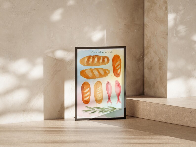May include: A framed watercolour print depicting several loaves of bread and two pink fish. The text "the wild provide" is at the top. The artwork is in a black frame, set against a neutral background.