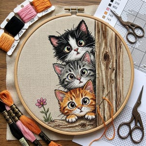 Può includere: Un telaio da ricamo rotondo in legno contenente un progetto a punto croce di tre gattini impilati verticalmente accanto a un palo di legno. I gattini sono bianco e nero, grigio tigrato e arancione tigrato. Include un piccolo fiore rosa.