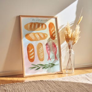 May include: Framed watercolour print depicting bread loaves, two pink fish, and green sprigs. The text "the will provide" is at the top. A clear glass vase with dried plants is to the right.