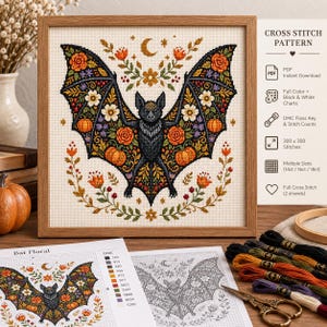 Può includere: Uno schema a punto croce con un pipistrello nero centrale circondato da zucche arancioni, fiori colorati e fogliame. Il disegno include una luna crescente e stelle. Lo schema è mostrato in una cornice di legno con istruzioni stampate.