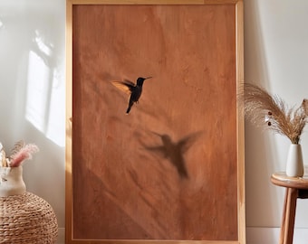 Pode incluir: Uma peça de arte de parede retangular numa moldura de madeira clara com um beija-flor escuro em voo contra um fundo sólido e texturizado de cor terracota. A obra apresenta uma sombra suave e desfocada da ave projetada por baixo.