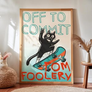 Op de afbeelding: Een ingelijste poster met een zwarte kat op een blauwgroen en oranje skateboard. De kat maakt een vredesteken met één poot. De tekst OFF TO COMMIT TOM FOOLERY staat in blauwgroene en oranje letters op een lichte achtergrond met stippen.
