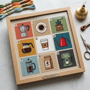 Op de afbeelding: Een ingelijste kruissteek sampler getiteld COFFEE LOVER'S SAMPLER - COLLECTION NO. 1, met negen genummerde vierkanten met geborduurde koffie-gerelateerde items zoals een moka pot, koffiekop, molen, karaf, beker, waterkoker, pers, zak en machine.
