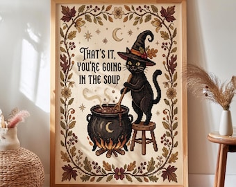 Könnte beinhalten: Ein gerahmtes Kreuzstichbild mit einer schwarzen Katze mit Hexenhut, die auf einem Hocker steht und in einem dampfenden Kessel rührt. Der Text lautet: "THAT'S IT, YOU'RE GOING IN THE SOUP". Das Motiv ist von herbstlichen Blättern und Blumen umrahmt.