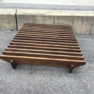 May include: A dark brown wooden coffee table with a slatted top and a simple, modern design. The table has a rectangular shape and is supported by four legs.