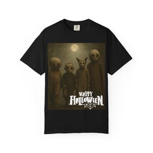 May include: A black short-sleeve t-shirt featuring a graphic print of four figures with round, mask-like heads standing under a full moon. The text "HAPPY HALLOWEEN" is printed in white below the figures, accompanied by a small spider web illustration.