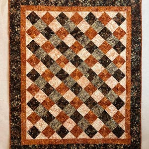 May include: A rectangular quilt featuring a diamond-patterned center composed of alternating squares in shades of dark brown, burnt orange, and cream with floral motifs. The quilt is framed by a burnt orange border and a dark floral outer border.