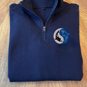 May include: A navy blue quarter-zip sweatshirt with an embroidered design of two orcas in a yin-yang symbol.