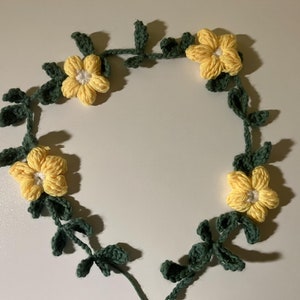 Peut inclure: Une couronne crocheté avec des fleurs jaunes et des feuilles vertes.