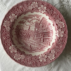 Peut inclure: Assiette ronde de style ancien avec une bordure florale rouge et blanche. Le centre présente une scène détaillée d'un village avec un bureau de poste, des personnes et des animaux. L'assiette est probablement en céramique.