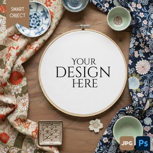 Pode incluir: Um bastidor de bordado de madeira com o texto "YOUR DESIGN HERE" é rodeado por tecido, pequenas tigelas e um prato decorativo. O tecido apresenta padrões florais em tons de vermelho, azul e bege. A imagem é uma maquete para colocação de design.