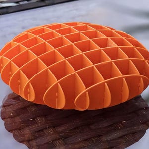 May include: Orange, 3D printed, geometric, sphere-shaped object with a grid pattern. The object is made of many small, connected, curved pieces.